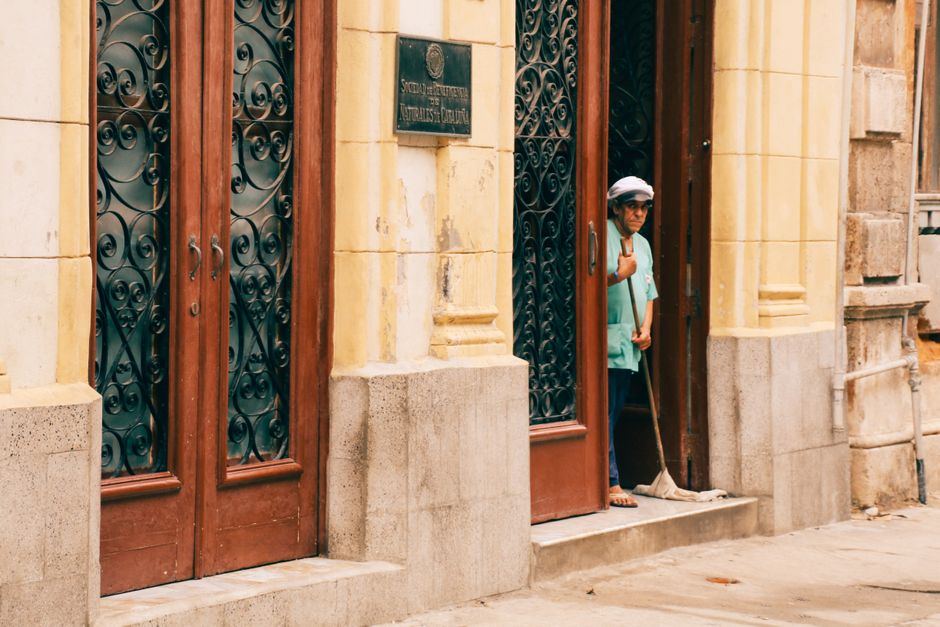 A person cleaning the entrance of a historic building with ornate doors, captured in an urban setting.